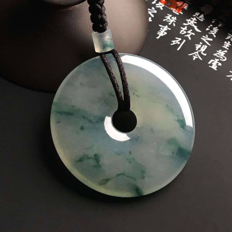 翡翠平安扣,也被称为翡翠怀古。翡翠平安扣的前身源于玉璧,玉璧是一种祭天的礼器,后经演变称为人们用来辟邪保平安的器具,并刻上一定的花纹,但是由于玉璧太大不易佩戴,人们便佩戴的是缩小版,尺寸变小不易刻上花纹,便又将其恢复为玉璧的模样,并取名为怀古,翡翠怀古由此而来。 冰种飘花平安扣挂件 翡翠平安扣的款式 通常,我们看见的传统的翡翠平安扣外形大体上类似于古铜钱,外圈是圆的,中间有小口,外形简单朴素,但是时下翡翠平安扣的款式也呈现了多样化,不仅仅限于常规的用绳子穿起的扁平圆状,还有其他的惹人喜爱的款式。 冰种